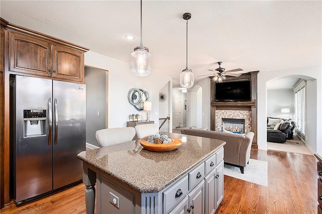 kitchen with arched walkways, light wood-style floors, a center island, and stainless steel fridge with ice dispenser