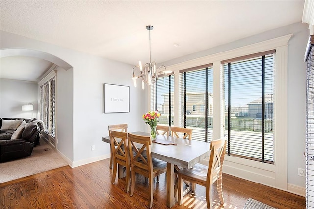 dining area featuring baseboards, arched walkways, light wood-style floors, and a chandelier