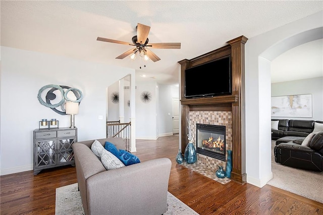 living room with arched walkways, a tile fireplace, baseboards, and wood finished floors