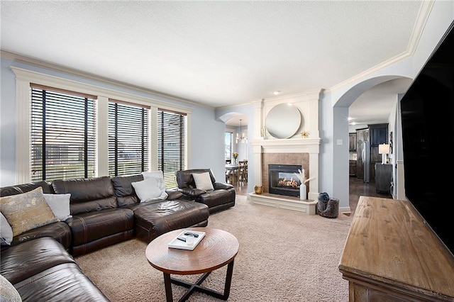 carpeted living area with arched walkways, a fireplace, crown molding, and baseboards