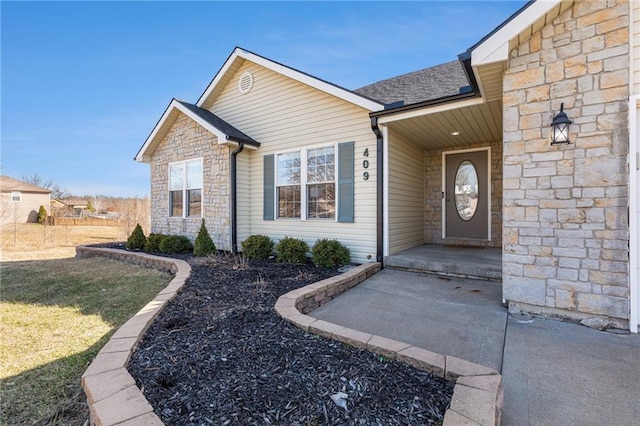 view of exterior entry featuring stone siding, a lawn, and a shingled roof