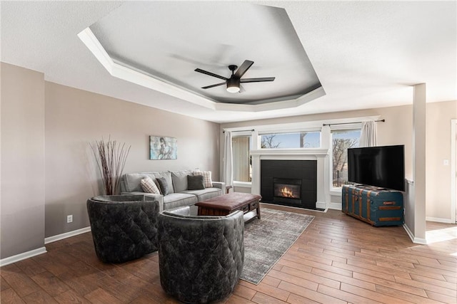 living area featuring ceiling fan, baseboards, a tray ceiling, and wood finished floors