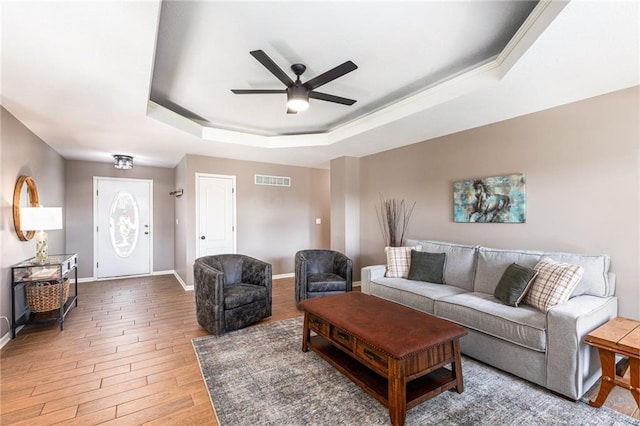 living room with visible vents, a tray ceiling, light wood-style floors, baseboards, and ceiling fan