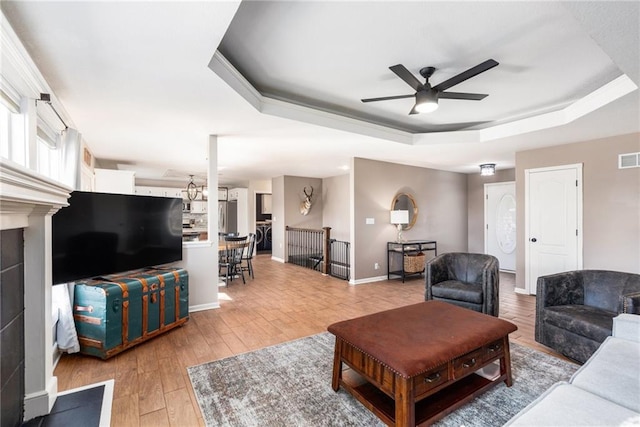 living room with a ceiling fan, baseboards, visible vents, a tray ceiling, and light wood-style flooring