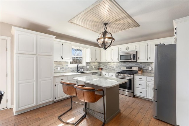 kitchen with wood finished floors, a sink, white cabinets, appliances with stainless steel finishes, and a center island