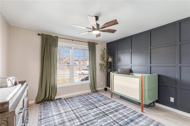 unfurnished bedroom featuring a decorative wall, a ceiling fan, baseboards, and light wood-style flooring