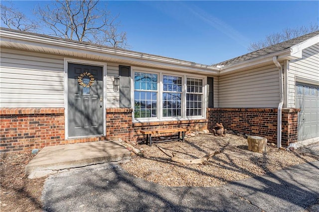 view of exterior entry with an attached garage and brick siding