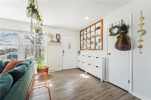 entrance foyer featuring visible vents, baseboards, a textured ceiling, and wood finished floors