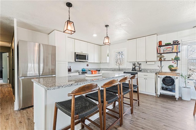 kitchen with white cabinetry, pendant lighting, light wood-type flooring, and stainless steel appliances