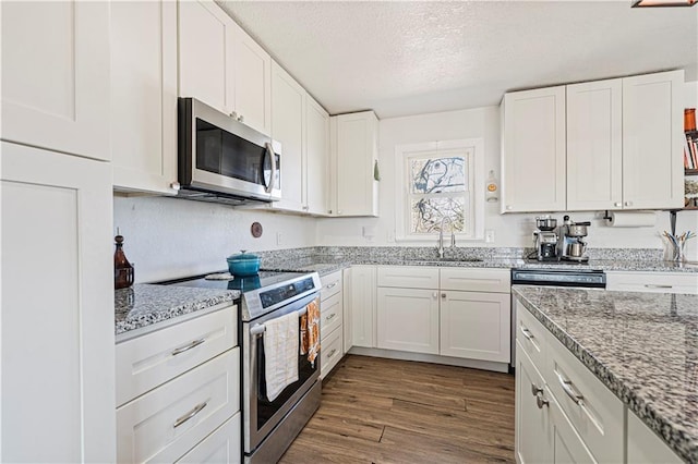 kitchen featuring a sink, a textured ceiling, wood finished floors, stainless steel appliances, and white cabinets