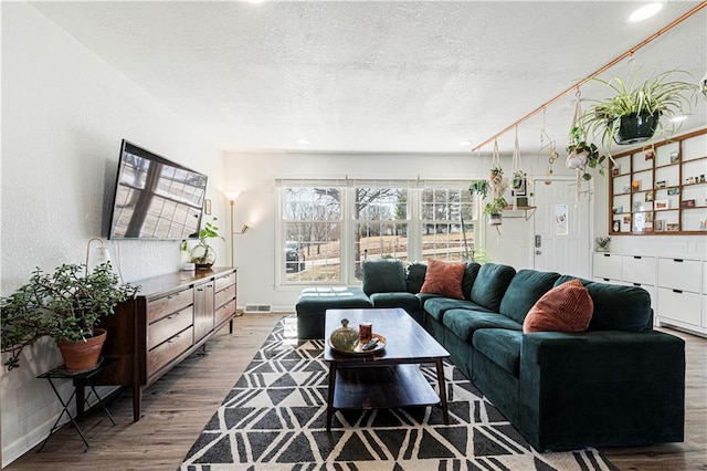 living room with visible vents, baseboards, a textured ceiling, and wood finished floors