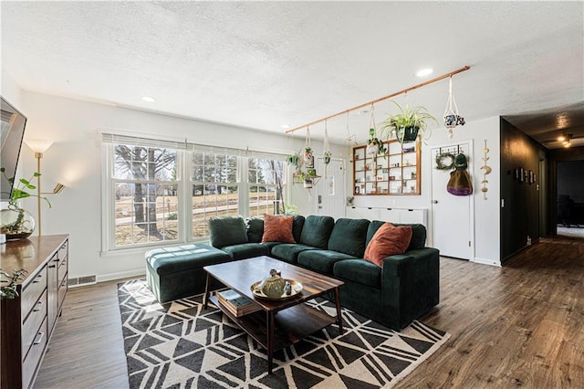 living area featuring visible vents, baseboards, a textured ceiling, and wood finished floors