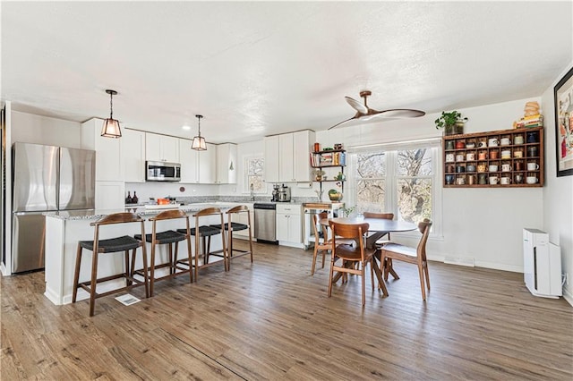 dining space featuring visible vents, ceiling fan, baseboards, wood finished floors, and a textured ceiling