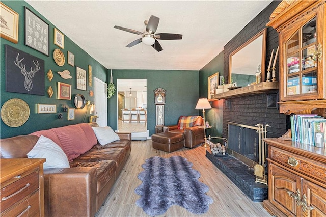 living room featuring a ceiling fan, a brick fireplace, and wood finished floors