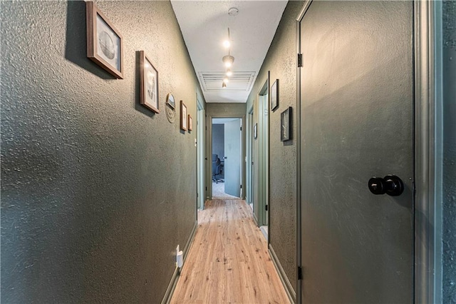 hall with visible vents, baseboards, light wood-style floors, and a textured wall