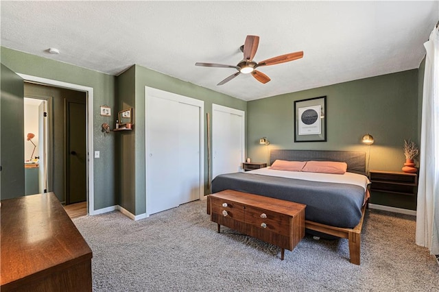 bedroom with two closets, baseboards, ceiling fan, carpet flooring, and a textured ceiling