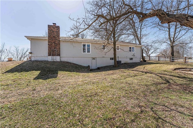 back of house featuring a lawn, a chimney, and fence