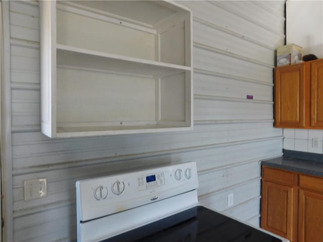 interior details featuring brown cabinets, open shelves, dark countertops, electric range oven, and wood walls