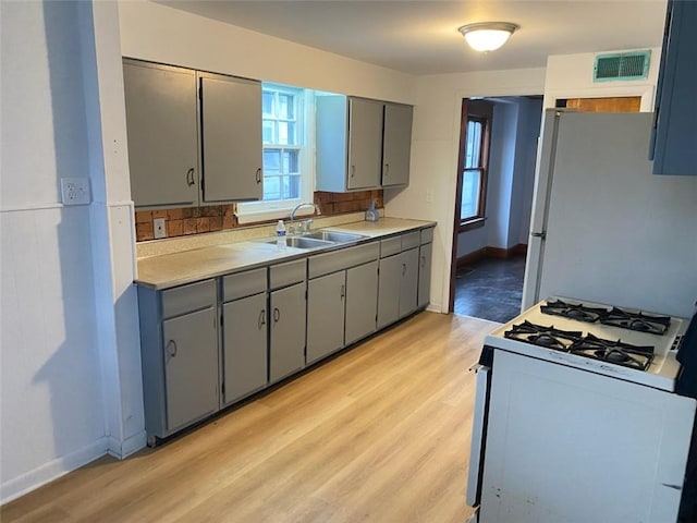 kitchen with light wood finished floors, visible vents, gray cabinets, white appliances, and a sink