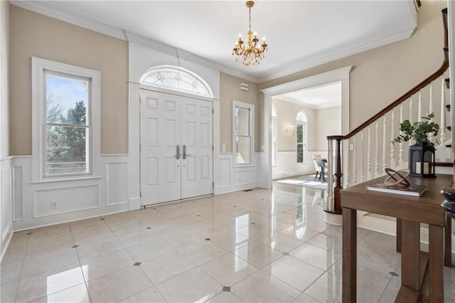 foyer featuring a decorative wall, crown molding, stairway, light tile patterned floors, and a notable chandelier