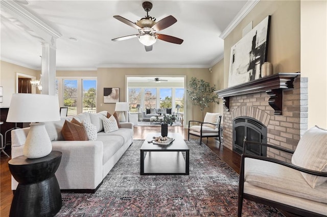 living area with ceiling fan, ornamental molding, decorative columns, a fireplace, and wood finished floors