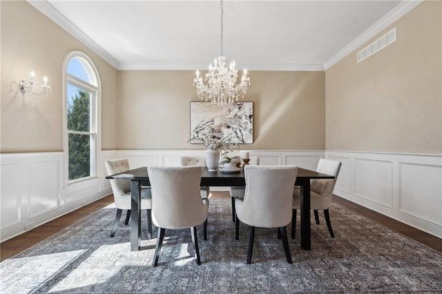 dining space featuring visible vents, ornamental molding, wood finished floors, an inviting chandelier, and wainscoting