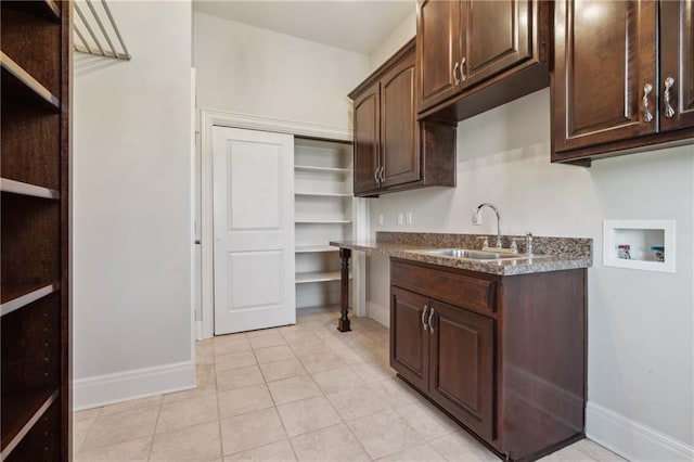 kitchen with dark brown cabinetry, light tile patterned floors, baseboards, and a sink