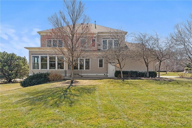 back of house featuring stucco siding and a yard