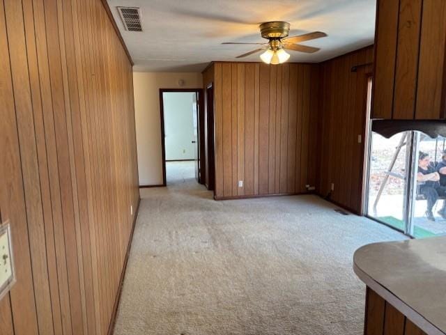 empty room featuring a ceiling fan, visible vents, wood walls, and light carpet