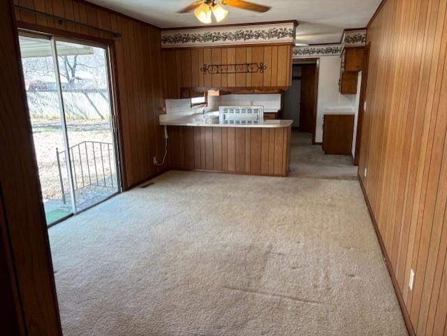 kitchen featuring wooden walls, light colored carpet, a peninsula, and brown cabinets