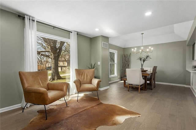 living area with visible vents, baseboards, an inviting chandelier, and hardwood / wood-style flooring