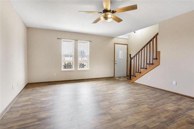 unfurnished living room featuring baseboards, a ceiling fan, wood finished floors, and stairs