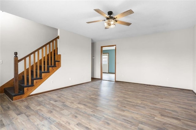 unfurnished living room with baseboards, stairs, ceiling fan, and wood finished floors