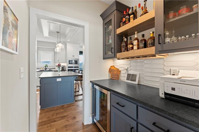 kitchen featuring a tray ceiling, stainless steel microwave, wine cooler, decorative backsplash, and dark wood-style flooring