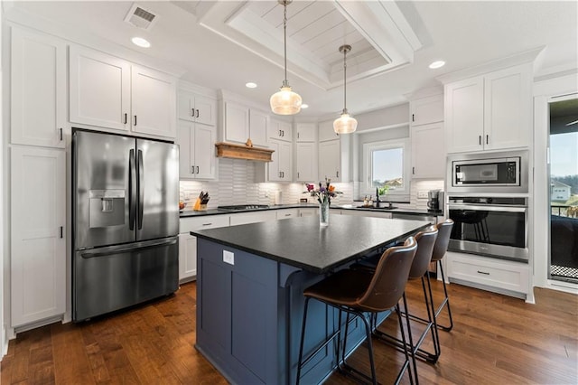 kitchen featuring dark countertops, appliances with stainless steel finishes, white cabinetry, a raised ceiling, and a sink