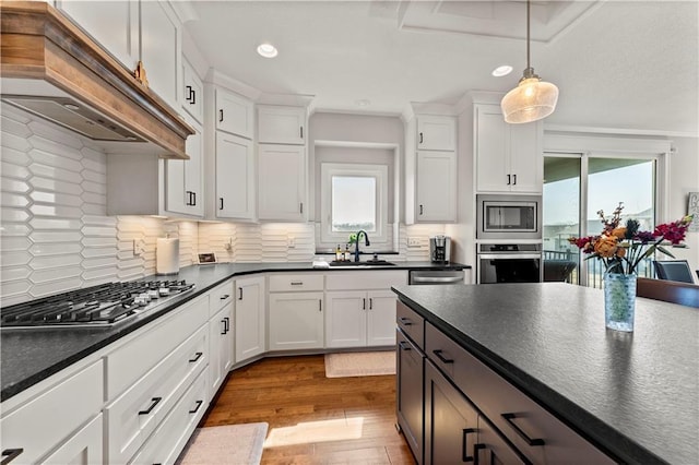 kitchen featuring under cabinet range hood, dark countertops, appliances with stainless steel finishes, and a sink