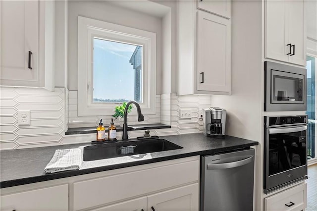 kitchen featuring a sink, appliances with stainless steel finishes, white cabinetry, dark countertops, and tasteful backsplash