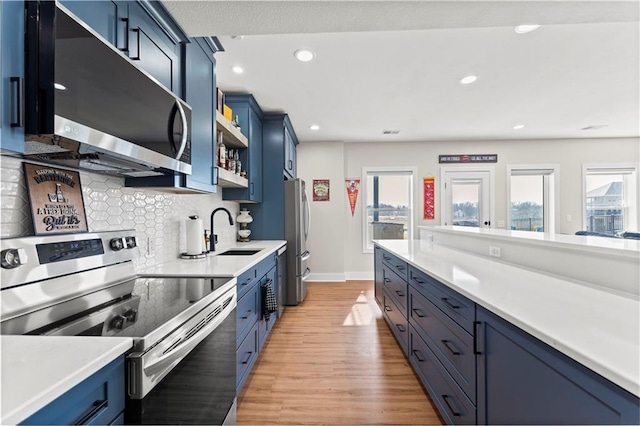 kitchen with open shelves, blue cabinetry, a sink, light countertops, and appliances with stainless steel finishes