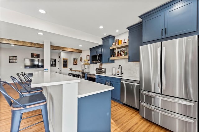 kitchen featuring blue cabinets, open shelves, a sink, a kitchen breakfast bar, and appliances with stainless steel finishes