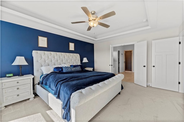 bedroom featuring a raised ceiling, light colored carpet, and ceiling fan