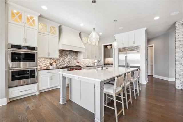 16121 Paradise St, Overland Park, KS 66221 - kitchen featuring appliances with stainless steel finishes, premium range hood, tasteful backsplash, white cabinets, and a kitchen breakfast bar