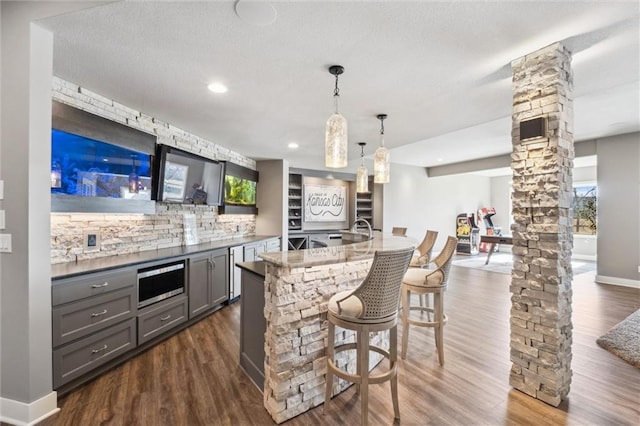 16121 Paradise St, Overland Park, KS 66221 - indoor bar with stainless steel microwave, backsplash, decorative columns, dark wood finished floors, and hanging light fixtures