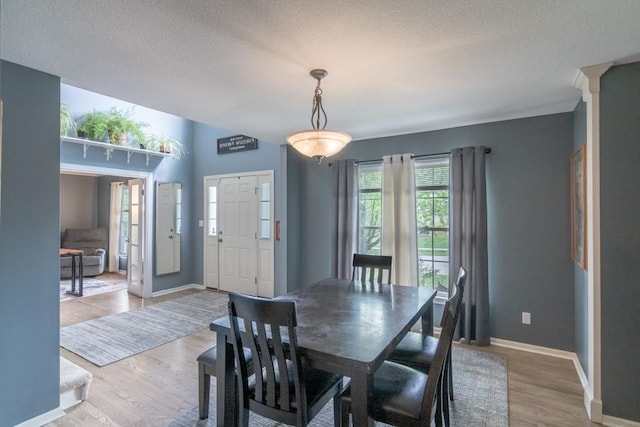 dining room featuring baseboards, a textured ceiling, light wood-style flooring, and decorative columns