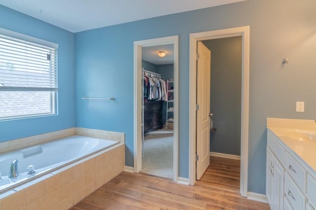 bathroom featuring a garden tub, wood finished floors, vanity, baseboards, and a spacious closet