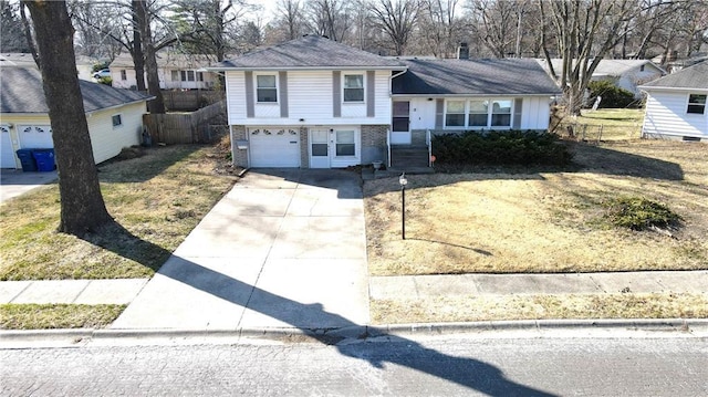 tri-level home featuring brick siding, driveway, a garage, and fence