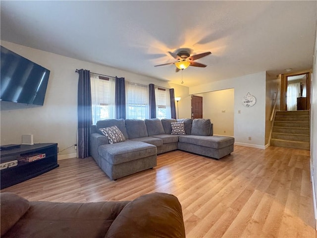 living area featuring light wood-type flooring, stairway, baseboards, and a ceiling fan