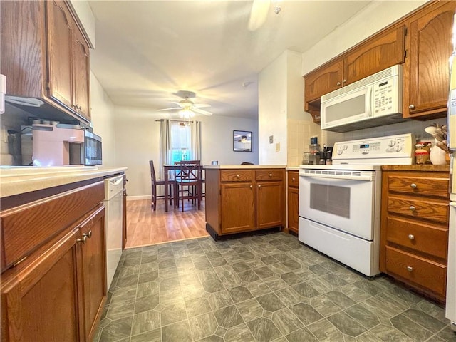 kitchen with white appliances, a peninsula, brown cabinetry, and light countertops