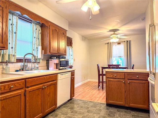 kitchen with a ceiling fan, a sink, brown cabinetry, light countertops, and dishwasher