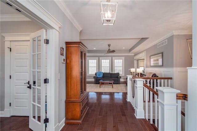 hallway featuring dark wood finished floors, visible vents, an upstairs landing, and ornamental molding