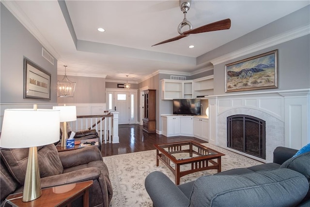 living area with visible vents, ornamental molding, a raised ceiling, a brick fireplace, and dark wood-style flooring